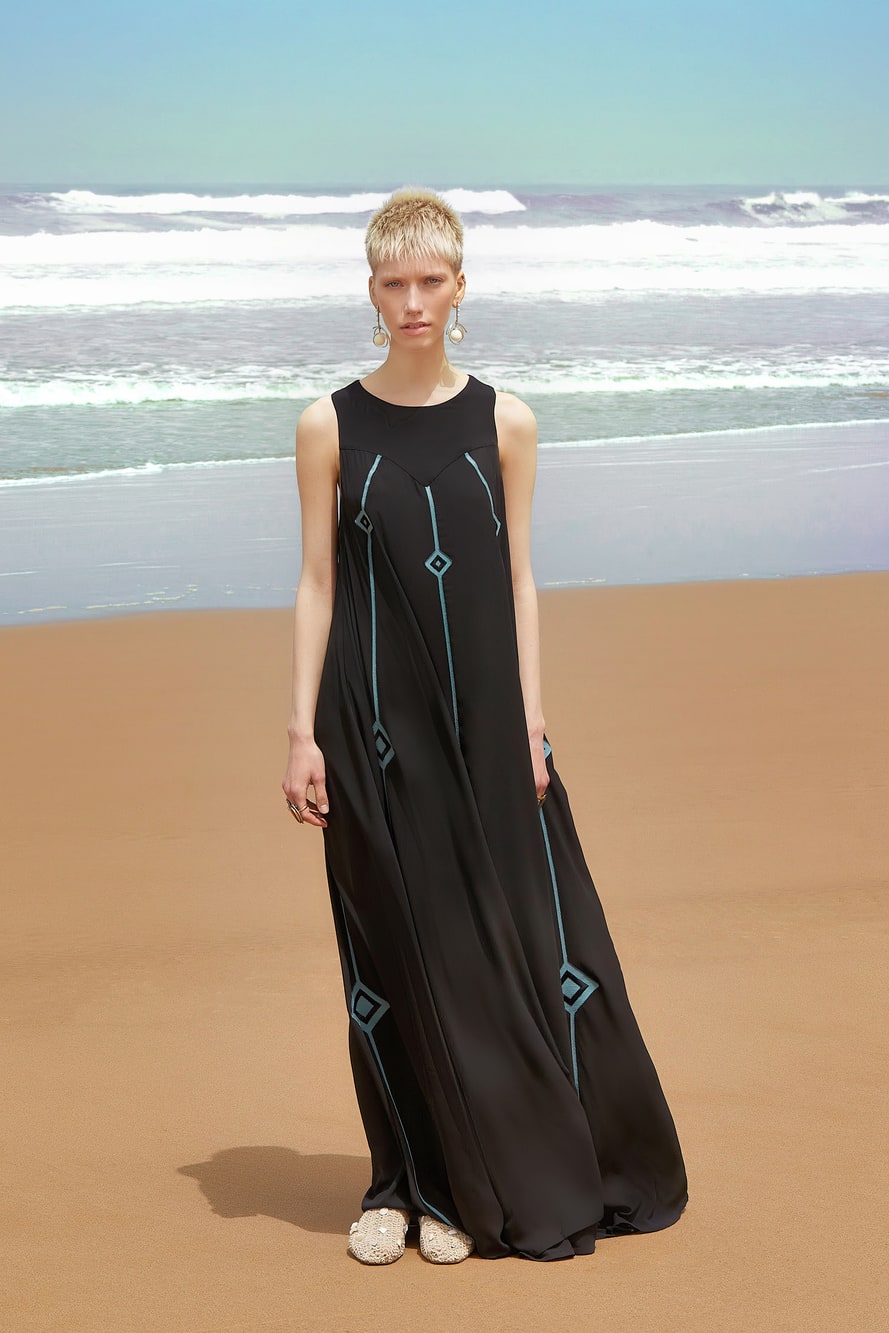 Woman in a black dress with geometric patterns standing on a beach.