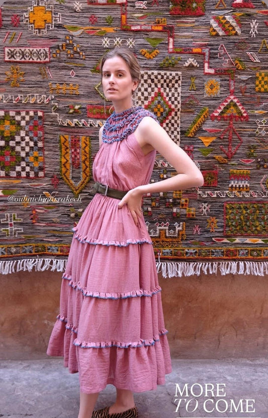 Woman in a pink dress standing in front of a colorful tapestry.